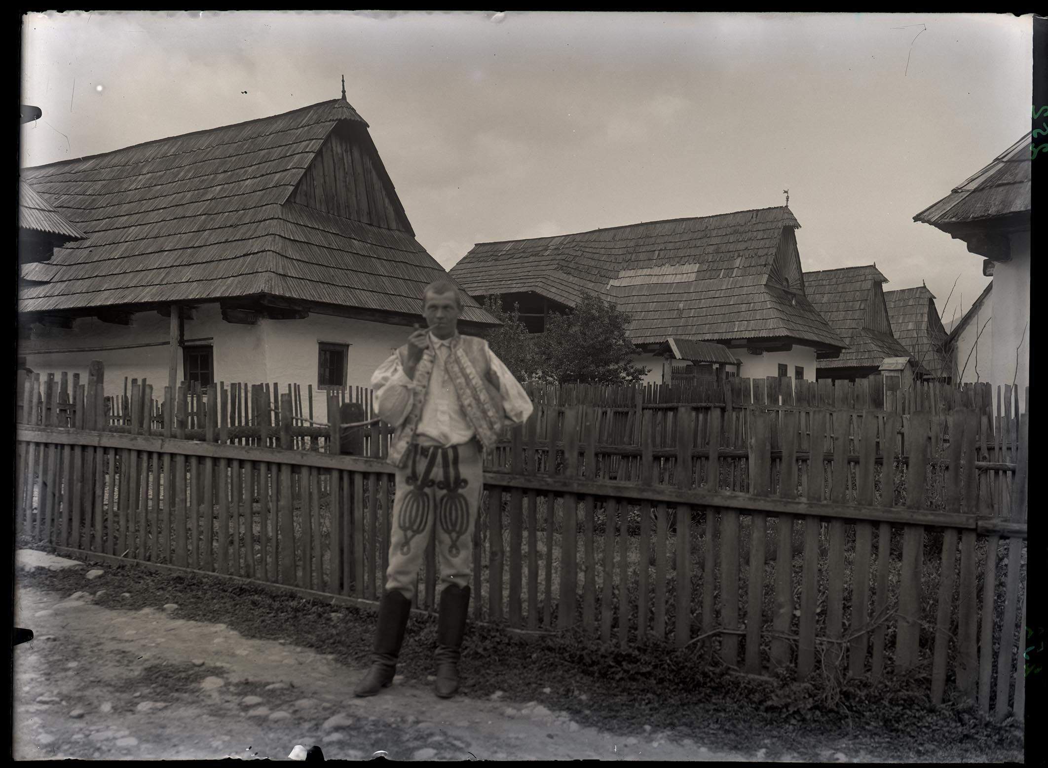 Náhledový obrázek Chalupy roubené ve Velké vsi, v popředí před plaňkovým plotem Ondřej Paclík v kroji s dýmkou, z č. 171. - 1