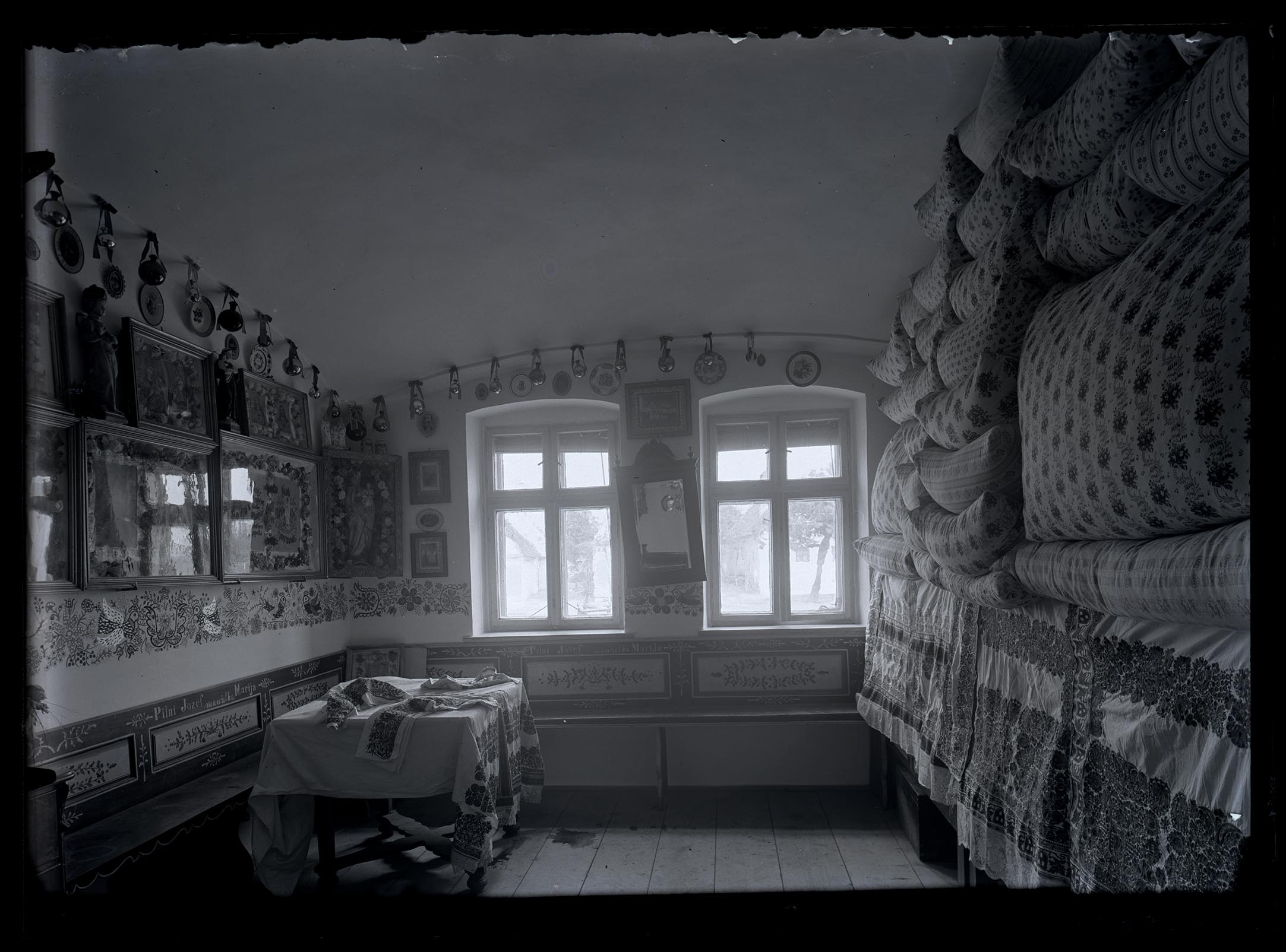 Náhledový obrázek Světnice v čp. 164. Na stole dvě výšivky, proti vyrovnané peřiny. Maj. Josef Pilný, svatý kout - 1